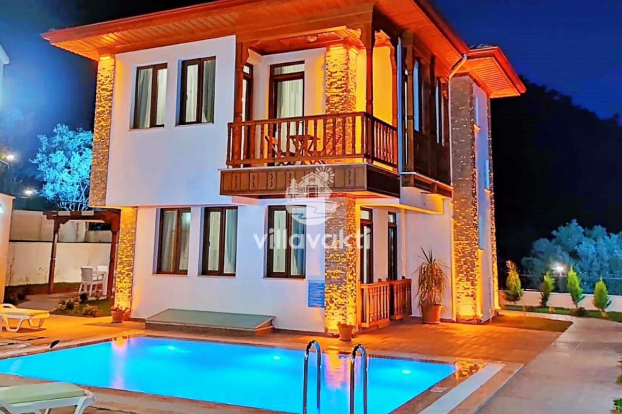Gece aydınlatmalı, havuzlu ve ahşap balkonlu iki katlı müstakil villa.
