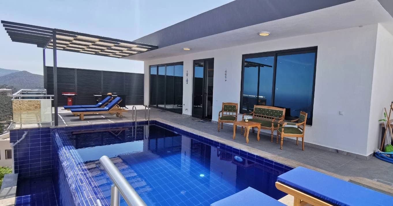 Havuz kenarında oturma grubu, şezlonglar ve modern villanın dış cephesi.