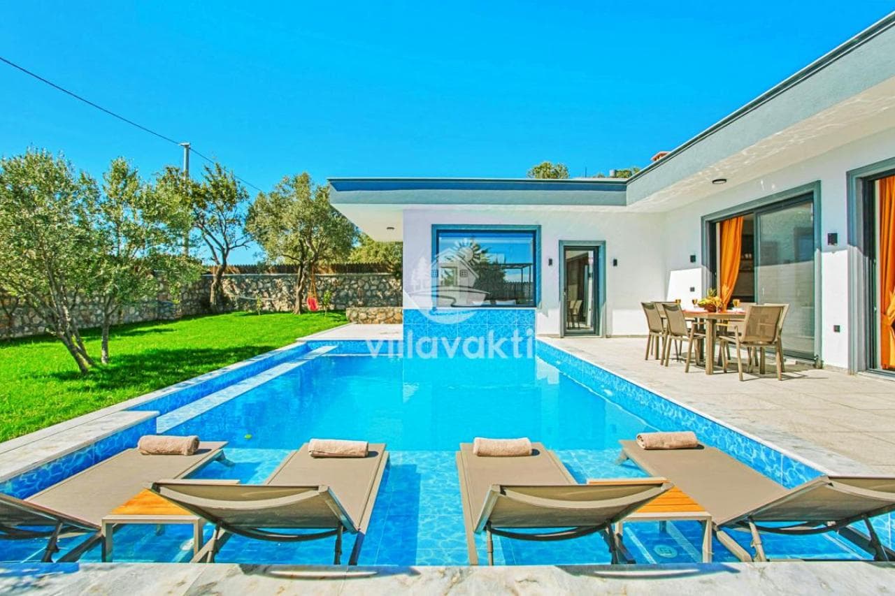 Havuz içinde şezlongların bulunduğu, bahçeli ve yemek masalı modern villa dış cephesi.