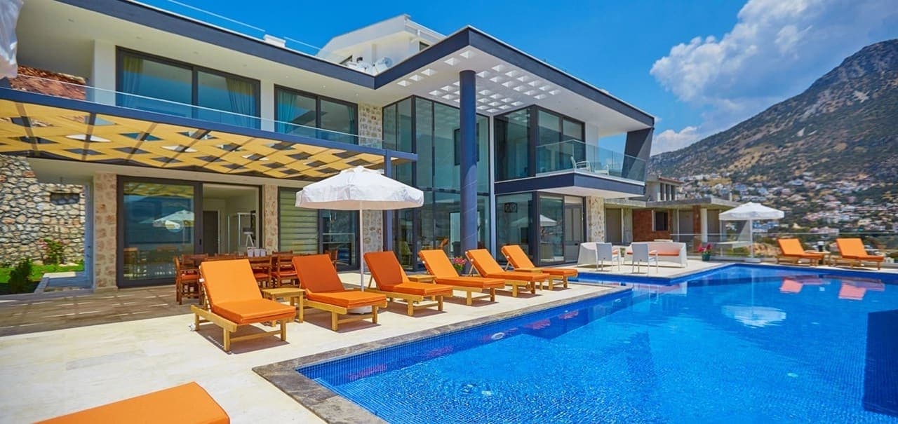 Modern mimariye sahip villa, önünde mavi havuz ve turuncu şezlonglar bulunan geniş bir teras.