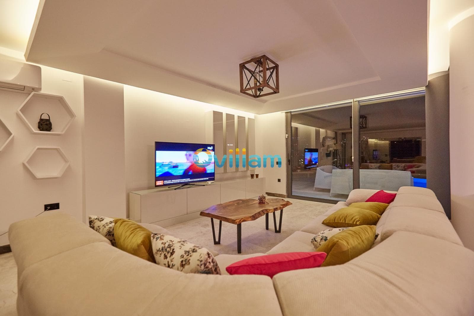 L şeklinde krem rengi koltuklar, ahşap orta sehpa ve televizyonun yer aldığı aydınlık salon.