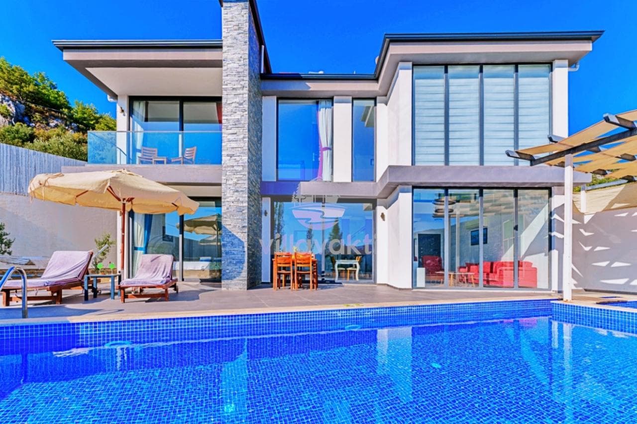 Modern mimariye sahip iki katlı villa, önünde mavi yüzme havuzu ve güneşlenme alanı.