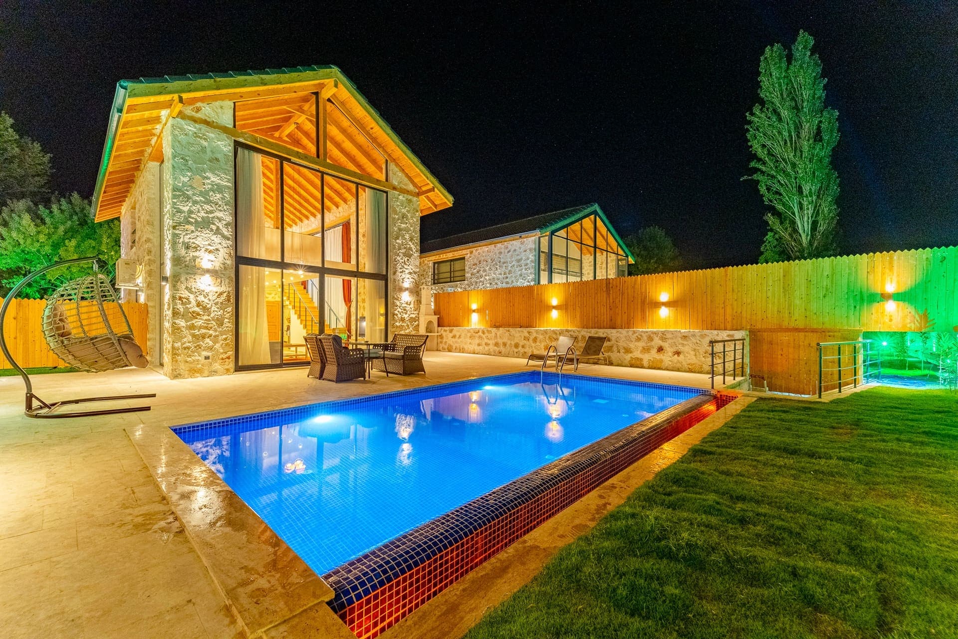 Gece aydınlatılmış taş villa, önünde havuz ve bahçe oturma alanı.