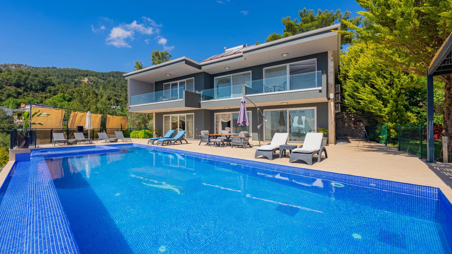 İki katlı modern gri villa, önünde şezlonglar ve geniş bir yüzme havuzu.