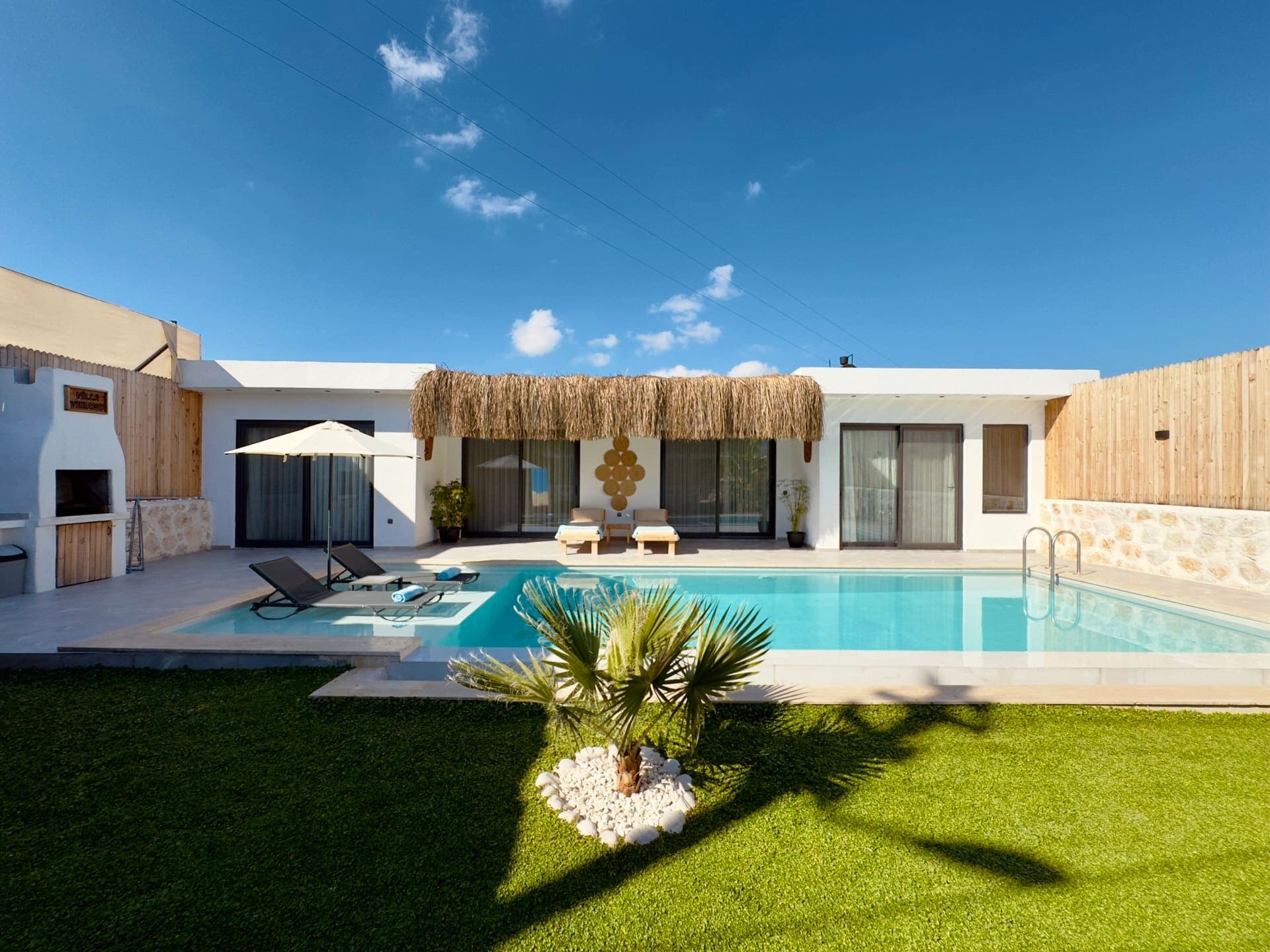 Villa Verano'nun açık yüzme havuzu, şezlong alanı ve çim bahçeli dış görünümü.
