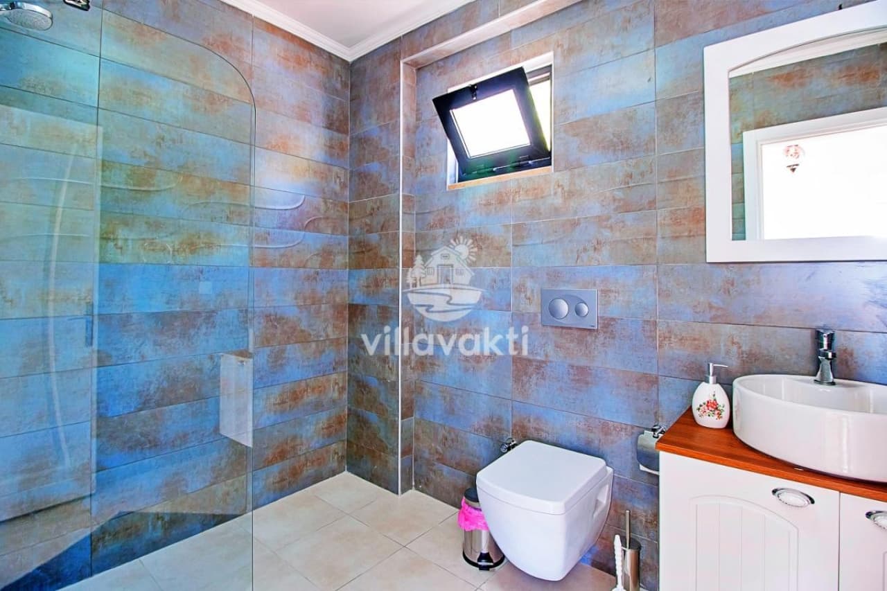 Desenli seramik duvarlara sahip, cam duş kabinli ve asma klozetli banyo.