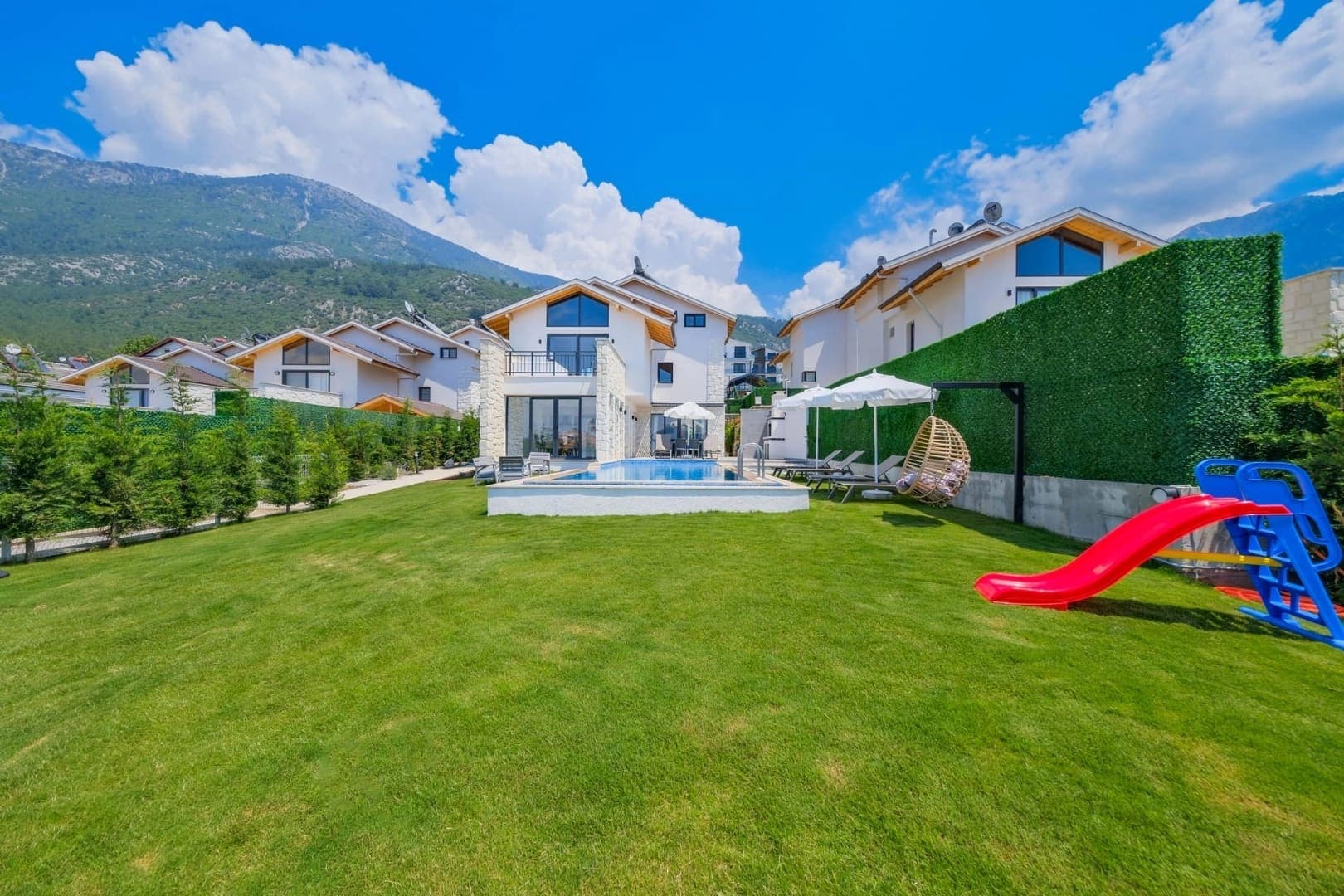 Geniş çim bahçesi, çocuk kaydırağı, salıncak ve yüzme havuzu olan modern villa.