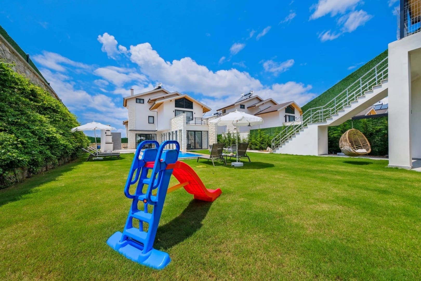 Bahçesinde çocuk kaydırağı, salıncak ve havuz bulunan yeşil alanlı villa bahçesi.
