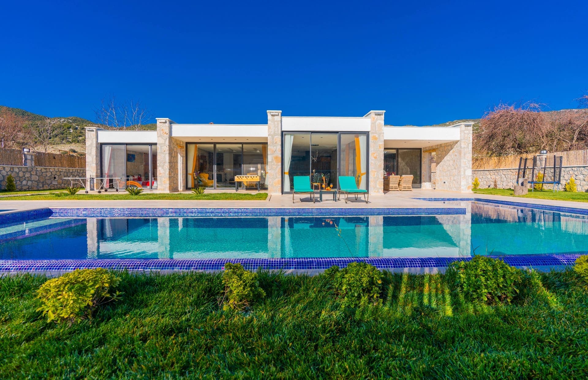 Önünde havuz bulunan, taş kaplamalı ve geniş camlı modern tek katlı villa dış cephesi.