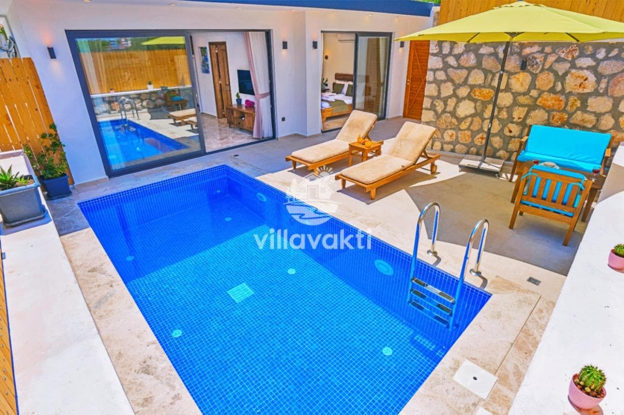 Özel yüzme havuzu, şezlonglar, sarı güneş şemsiyesi ve taş duvarlarla çevrili villa bahçesi.