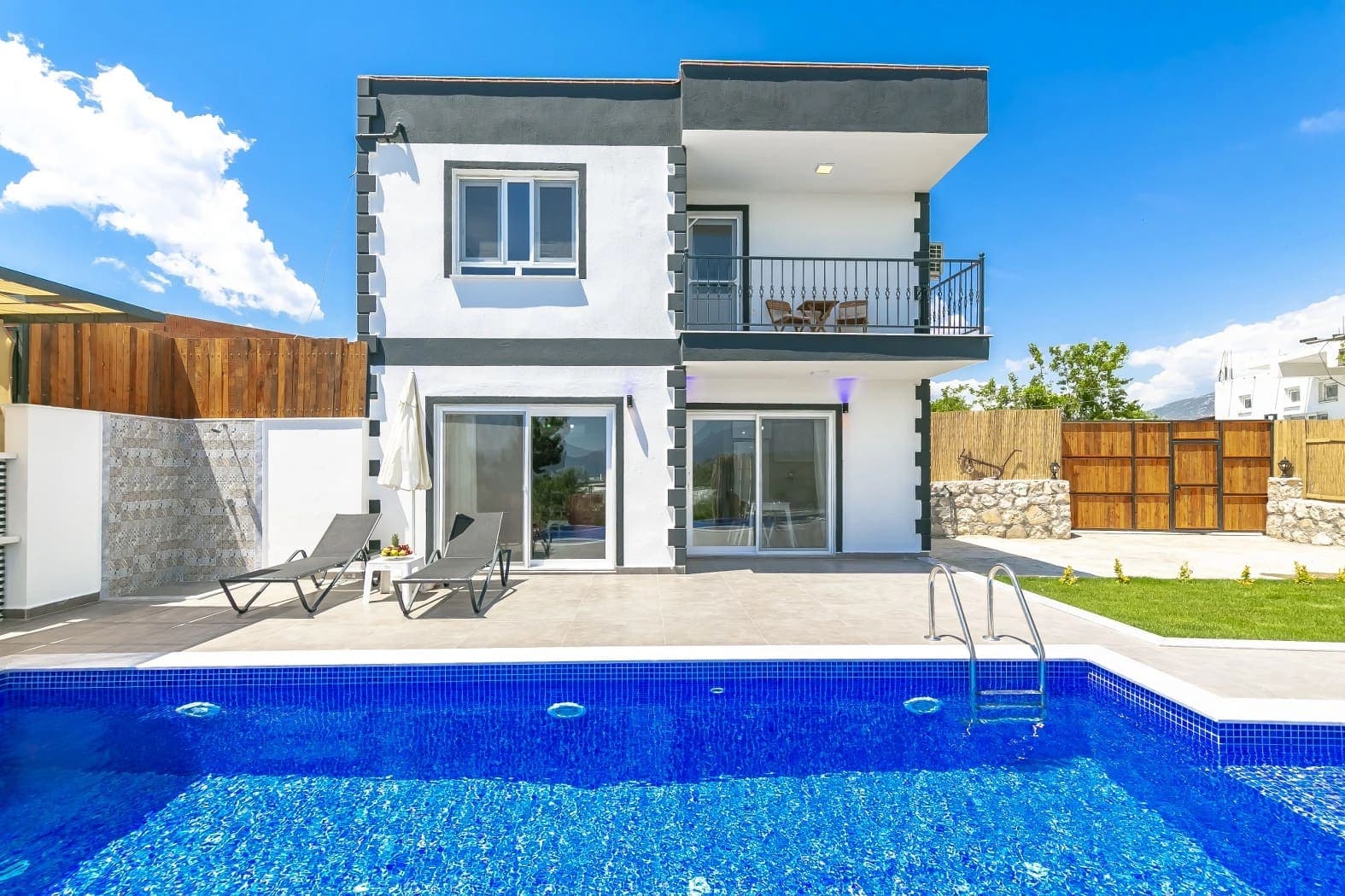 Siyah beyaz modern villa, önünde mavi havuz, şezlonglar ve geniş bir teras alanı.