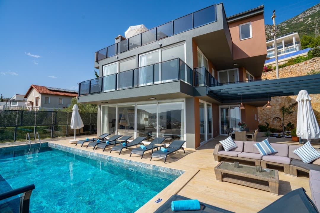 Önünde havuz, şezlonglar ve oturma grubu olan modern gri ve kahverengi villa.