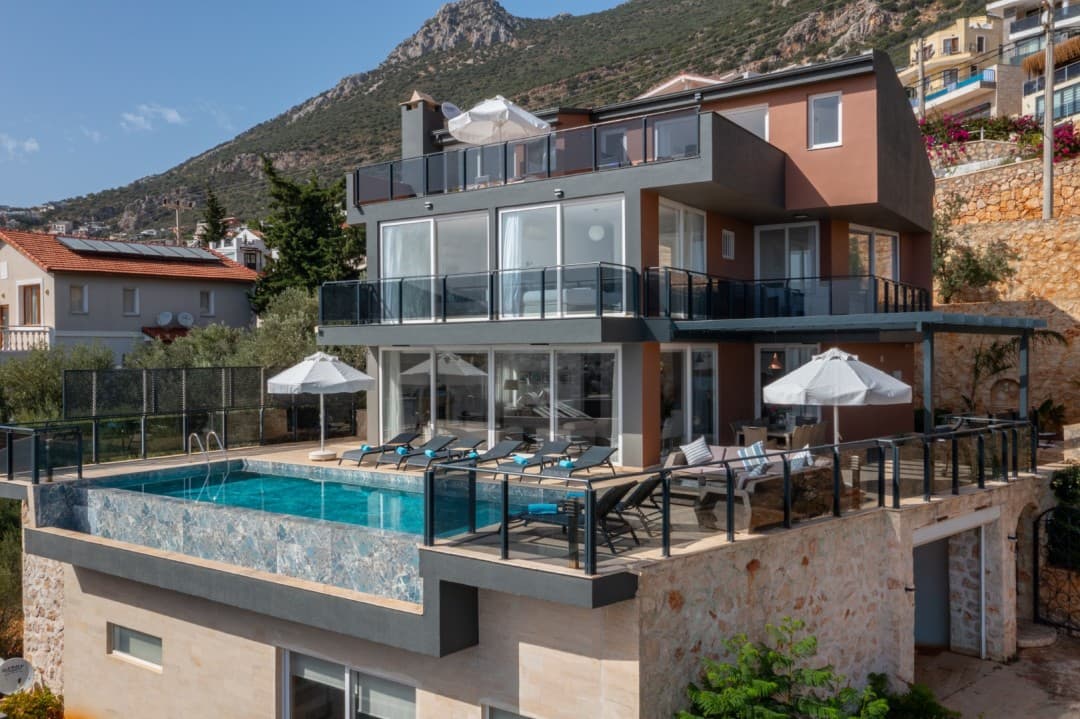 Dağ yamacındaki terasta yer alan sonsuzluk havuzu ve şezlonglu çok katlı villa.