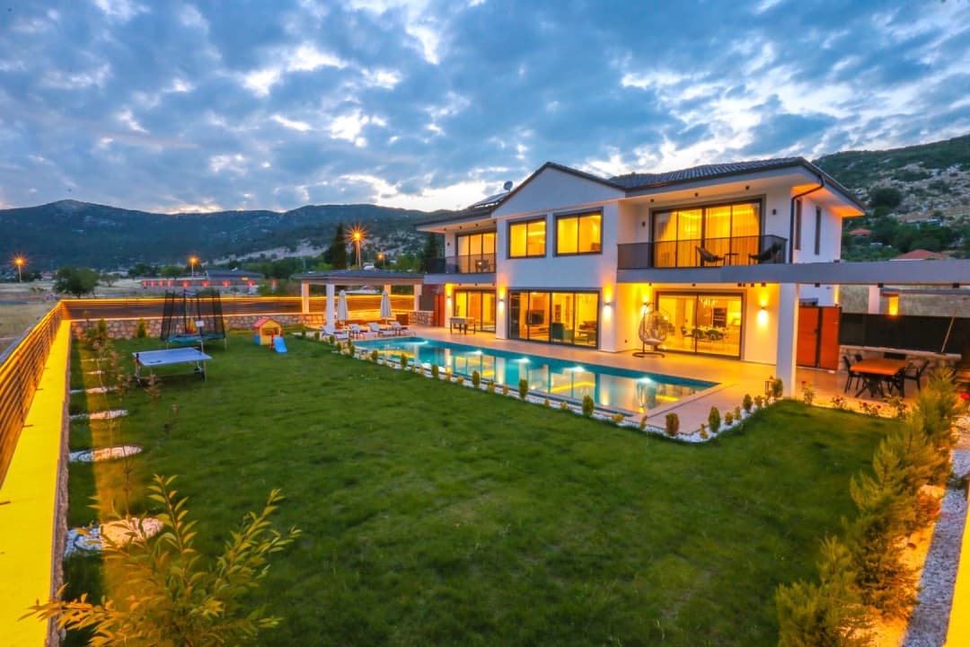 Alacakaranlıkta dış aydınlatmaları yanmış, havuzlu ve bahçeli iki katlı villa.