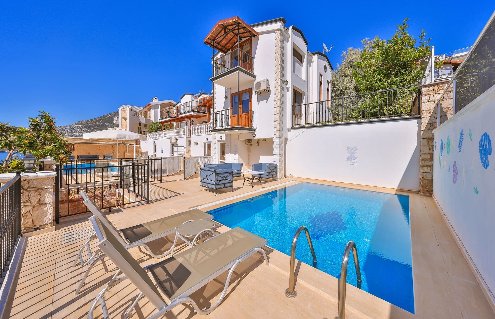 Önünde özel yüzme havuzu ve şezlonglar bulunan çok katlı beyaz villa.