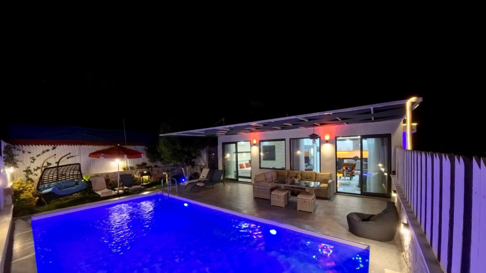 Gece aydınlatmalı havuz kenarında oturma grubu bulunan tek katlı villa.