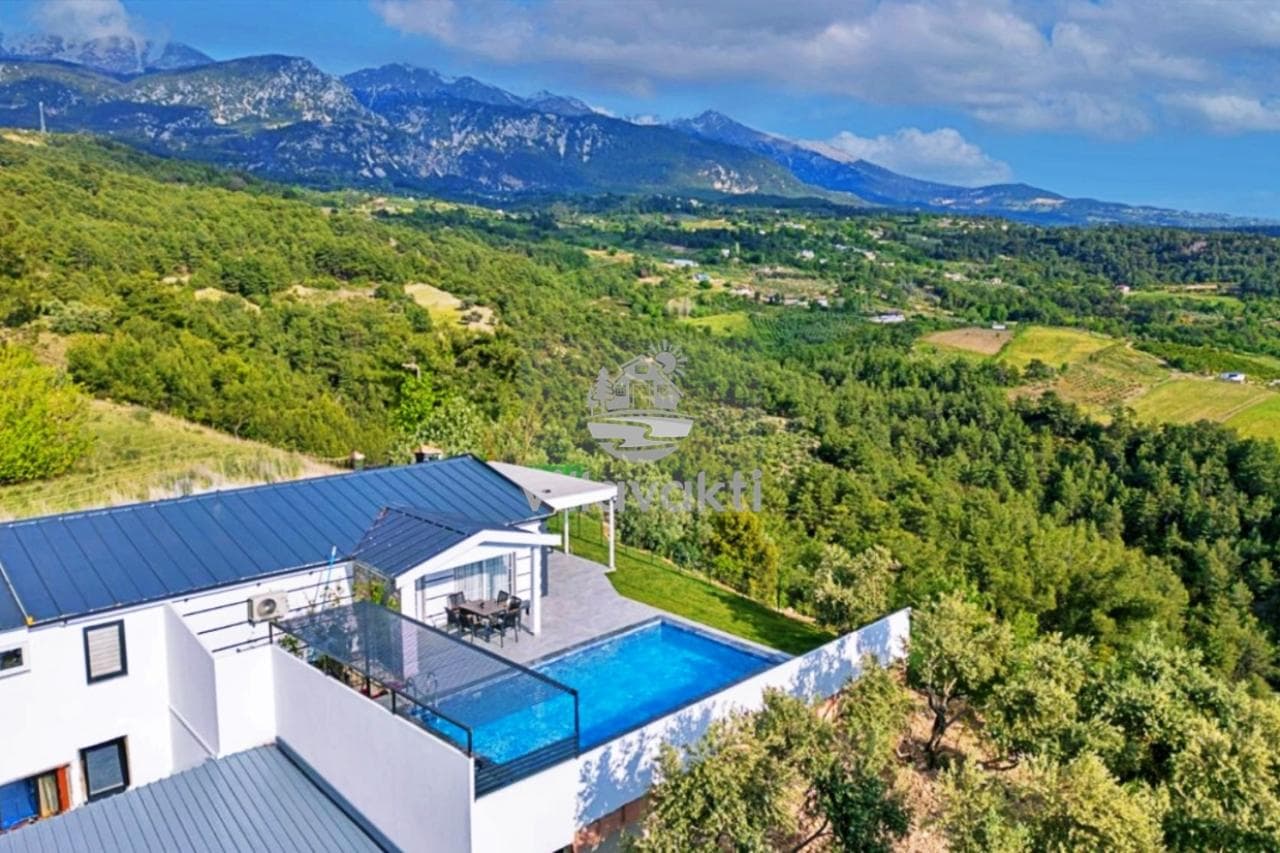 Yemyeşil ağaçlar ve dağ manzarasına karşı konumlanmış, özel havuzlu beyaz bir villa.