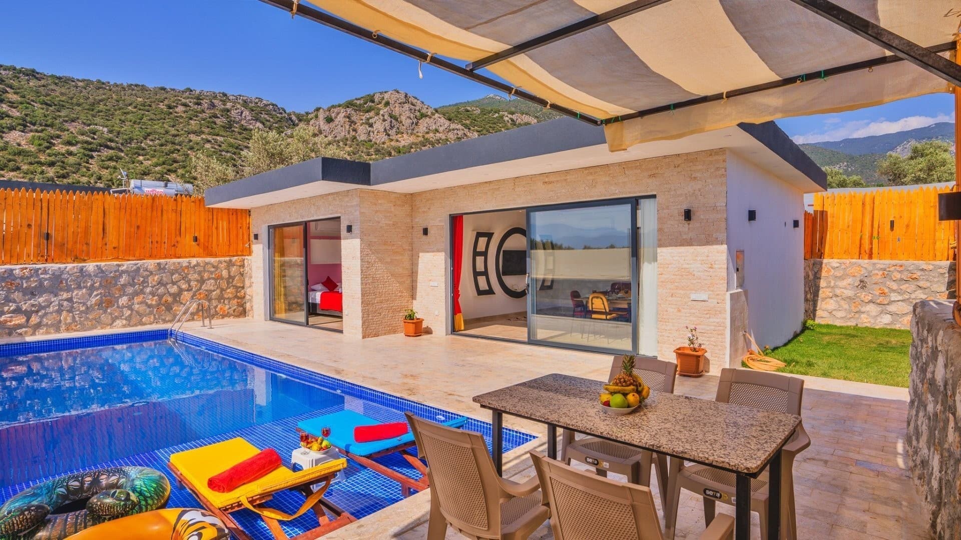 Önünde havuzu, güneşlenme şezlongları ve dış mekan yemek masası bulunan taş kaplamalı tek katlı villa.