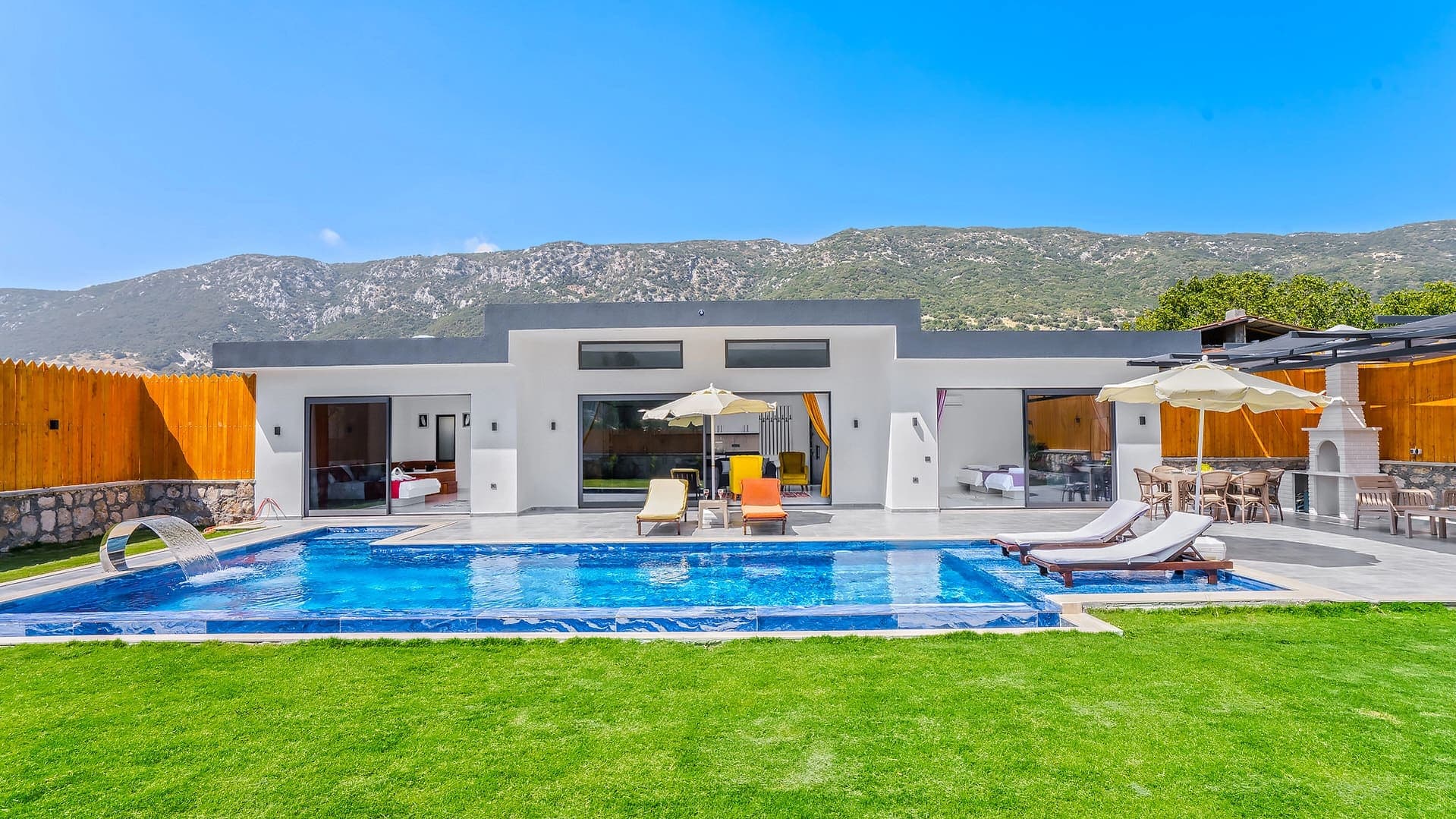 Dağ manzaralı, özel havuzlu, şezlonglu ve bahçeli tek katlı villa dış cephesi.