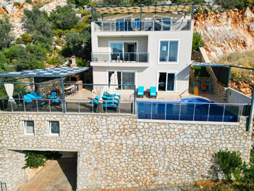 Taş duvarlı, üç katlı, havuzlu ve güneşlenme terasında şezlonglar bulunan modern villa.