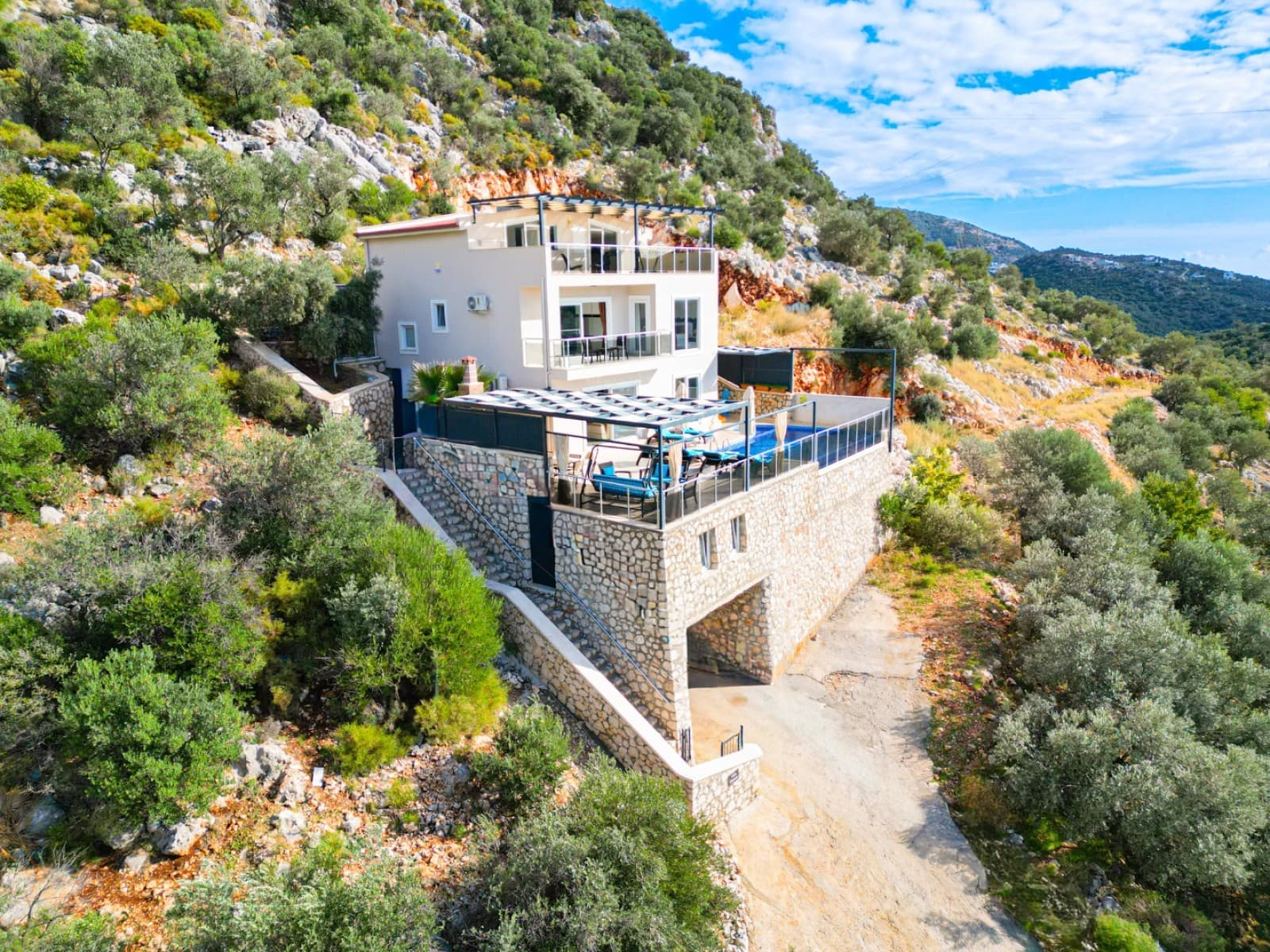 Yamaç üzerine kurulu, taş kaplama alt katı ve teraslı havuzu olan üç katlı villa.