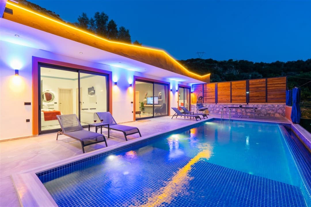 Gece mavi ve sarı ışıklarla aydınlatılmış havuzlu modern villa cephesi.