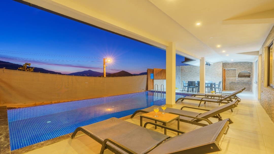 Geniş terasta havuz kenarına dizilmiş şezlonglar ve sehpa üzerinde bardaklar bulunan villa dış alanı.