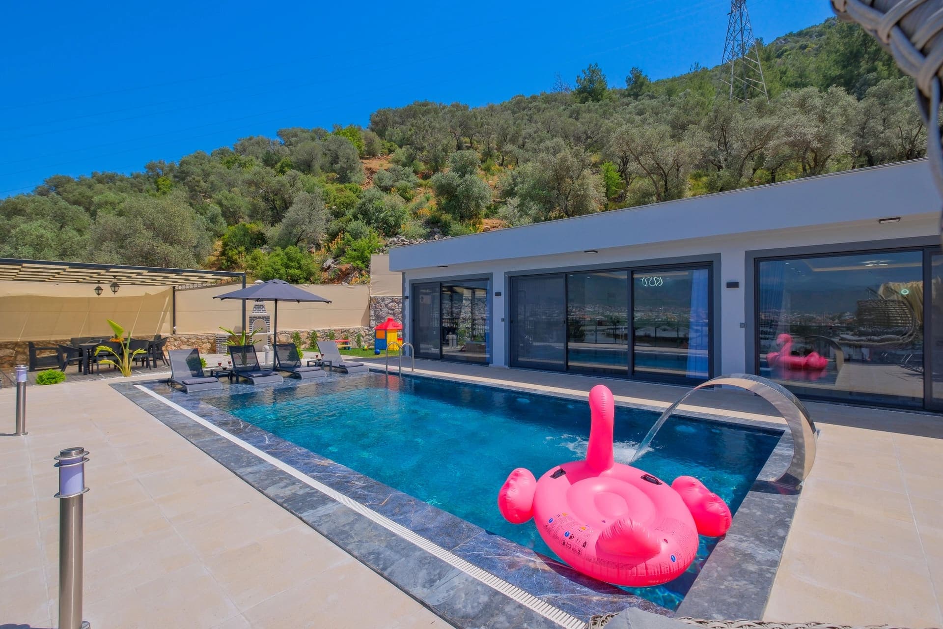Pembe deniz yatağı, şezlonglar ve arka planda dağ manzarası olan yüzme havuzlu villa.