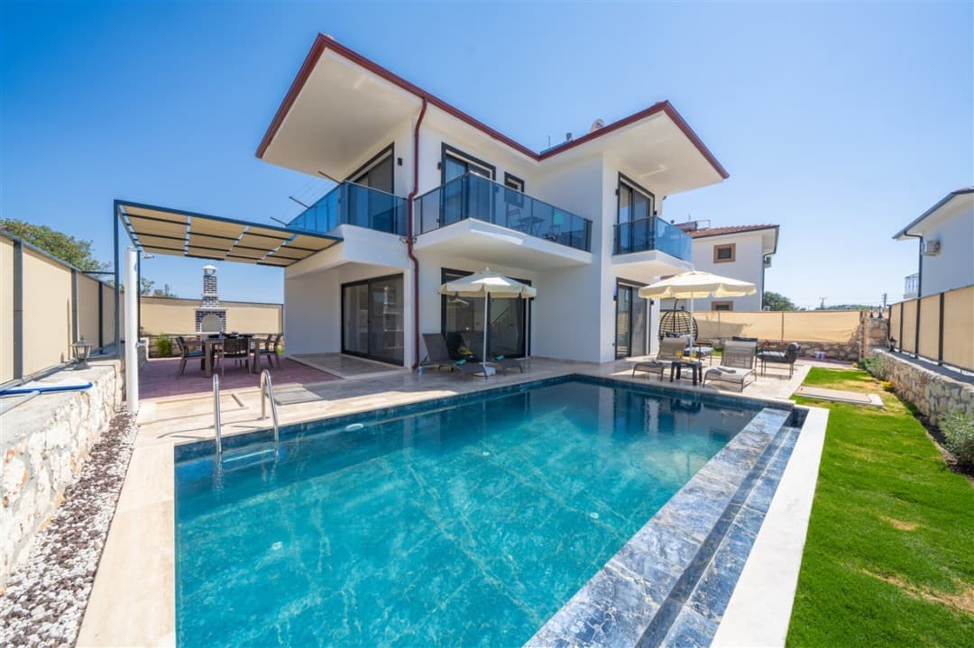 Önünde havuzu ve şezlongları olan iki katlı beyaz villa.