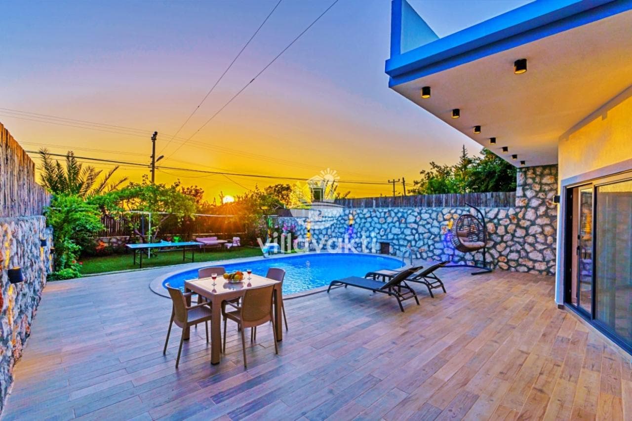 Gün batımında açık yüzme havuzu, yemek masası ve salıncağın yer aldığı veranda.