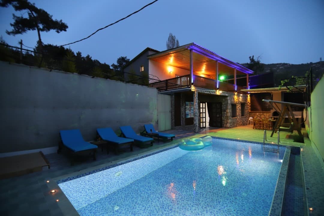 Akşam vakti aydınlatılmış havuzu ve şezlongları olan iki katlı taş villa.