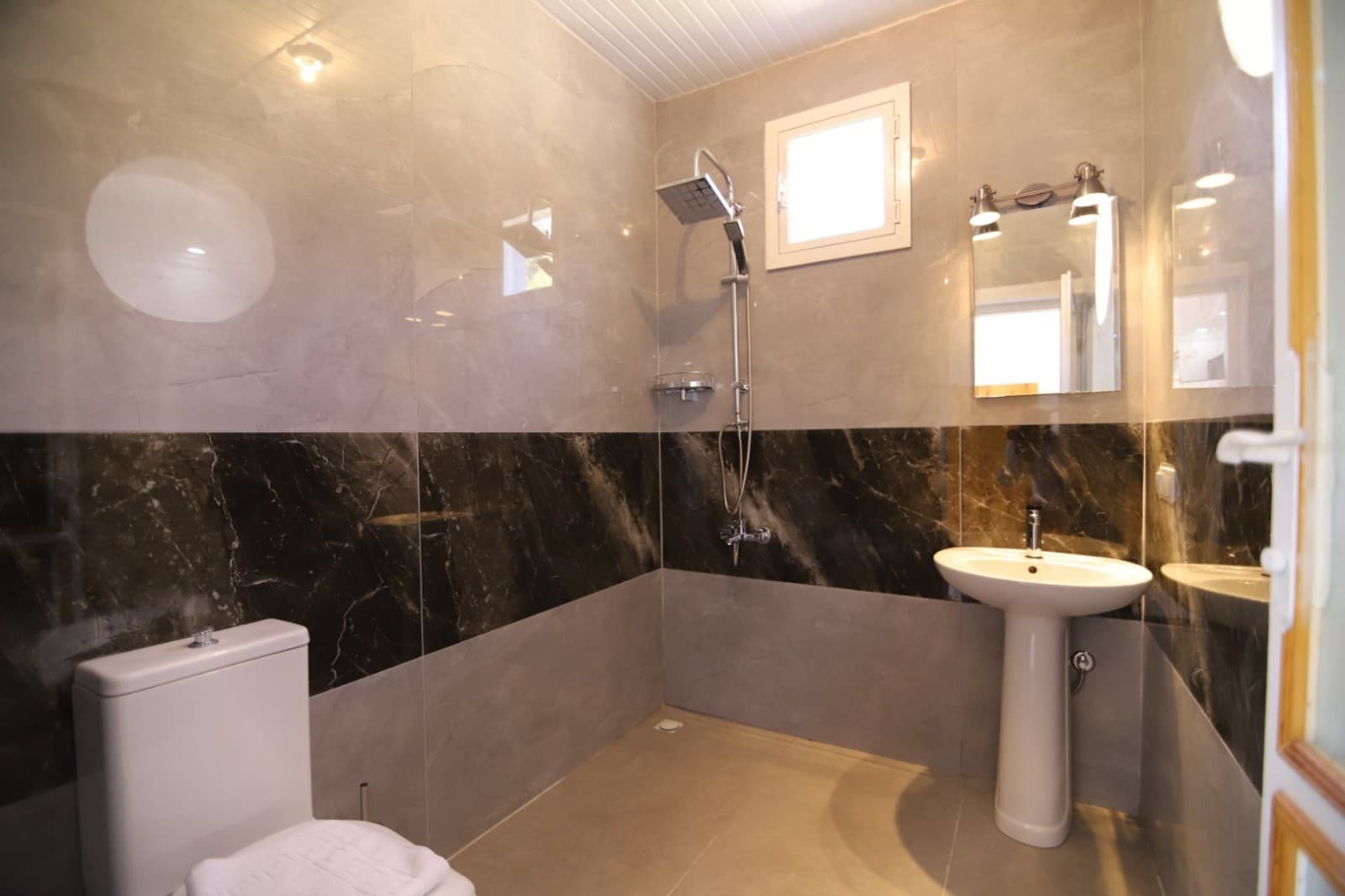 Gri mermer kaplı banyoda duş başlığı, lavabo ve tuvalet yer alıyor.
