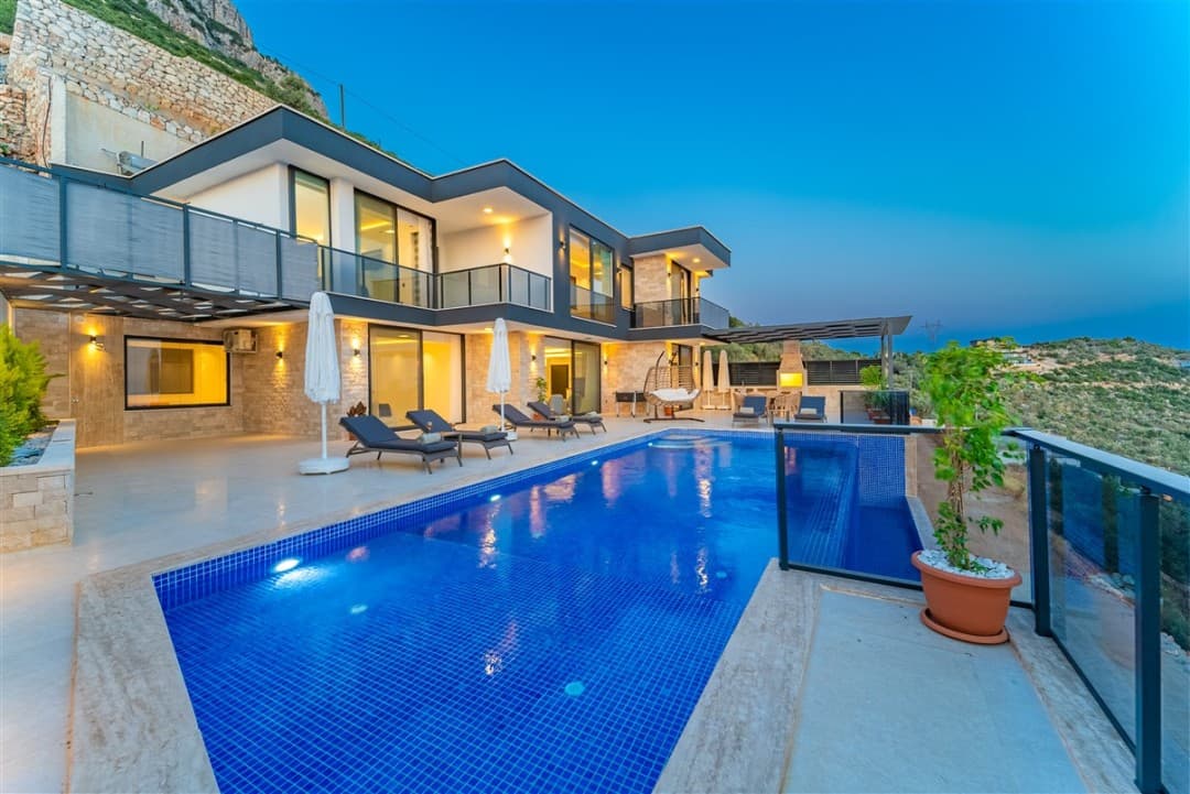 Alacakaranlıkta havuz başı şezlongları ve modern iki katlı villa.