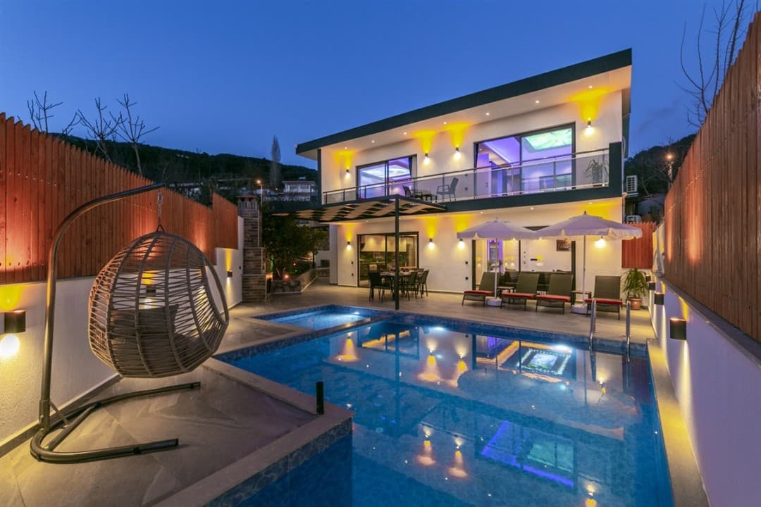Akşam aydınlatmalı, havuzlu ve bahçesinde salıncak bulunan iki katlı modern villa.