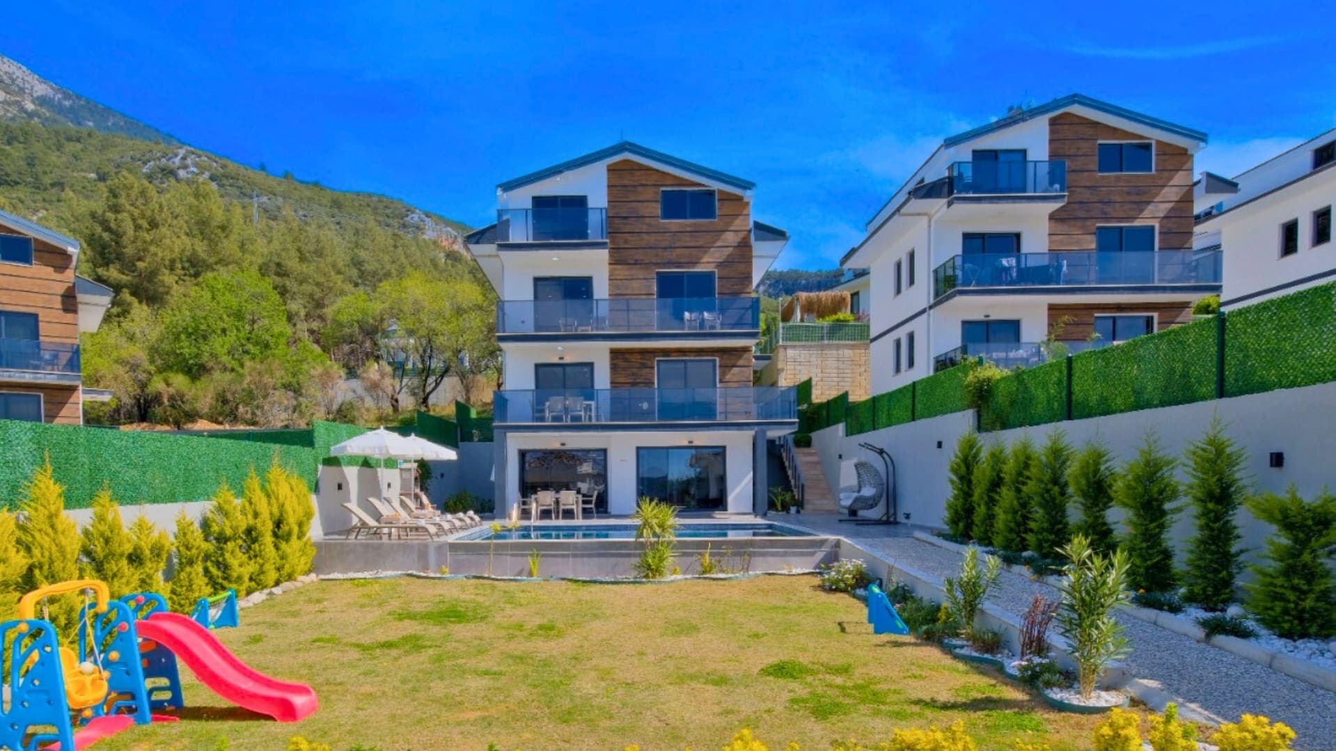 Bahçesinde çocuk oyun alanı, özel havuzu ve şezlongları bulunan üç katlı modern villa.