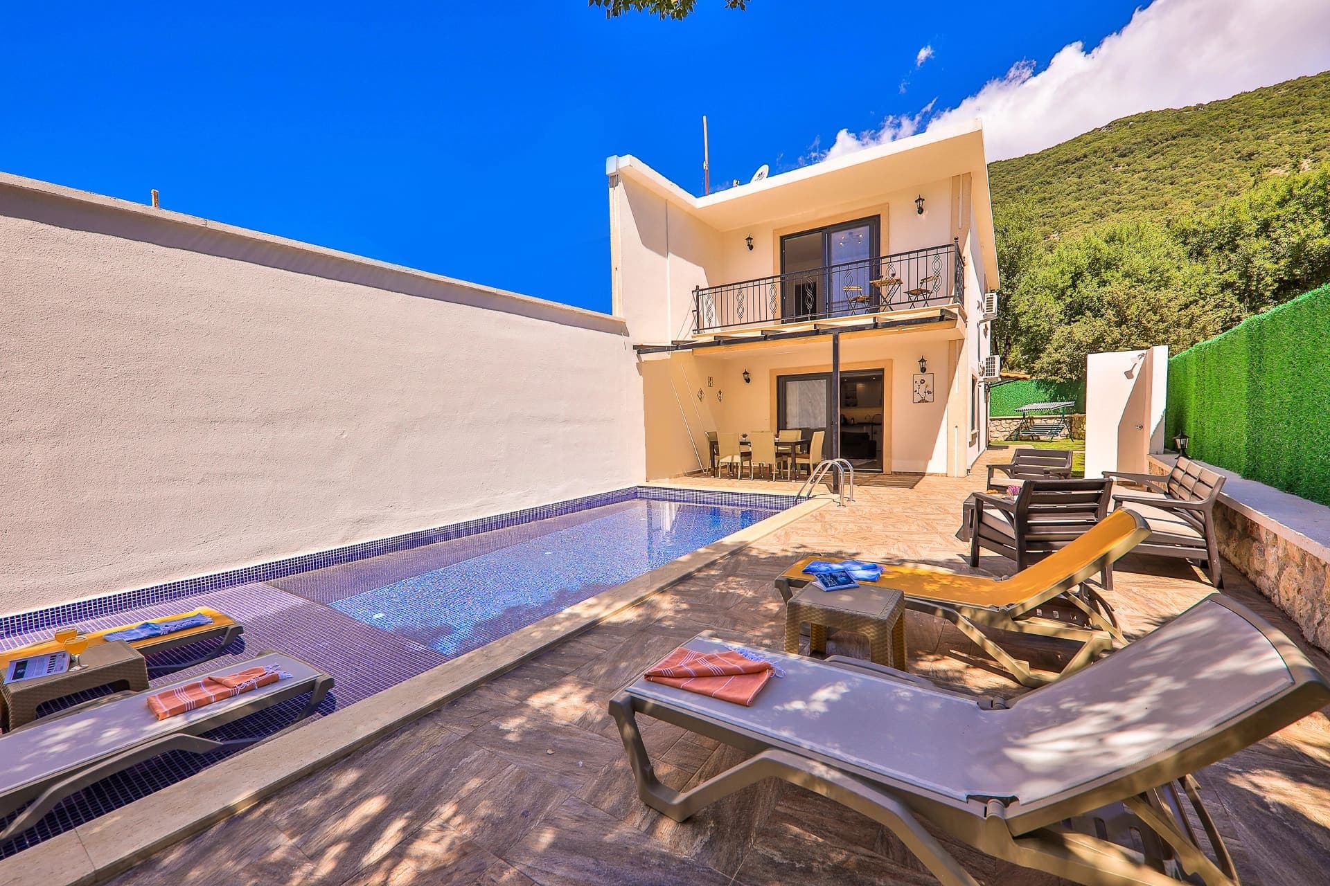 Özel yüzme havuzu, şezlonglar ve balkonlu iki katlı villa dış cephesi.