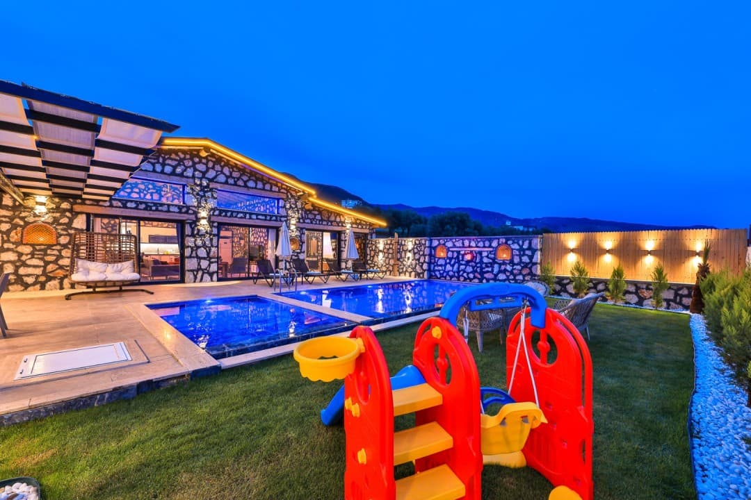Akşam vakti çocuk oyun parkı bulunan havuzlu ve taş cepheli villa.