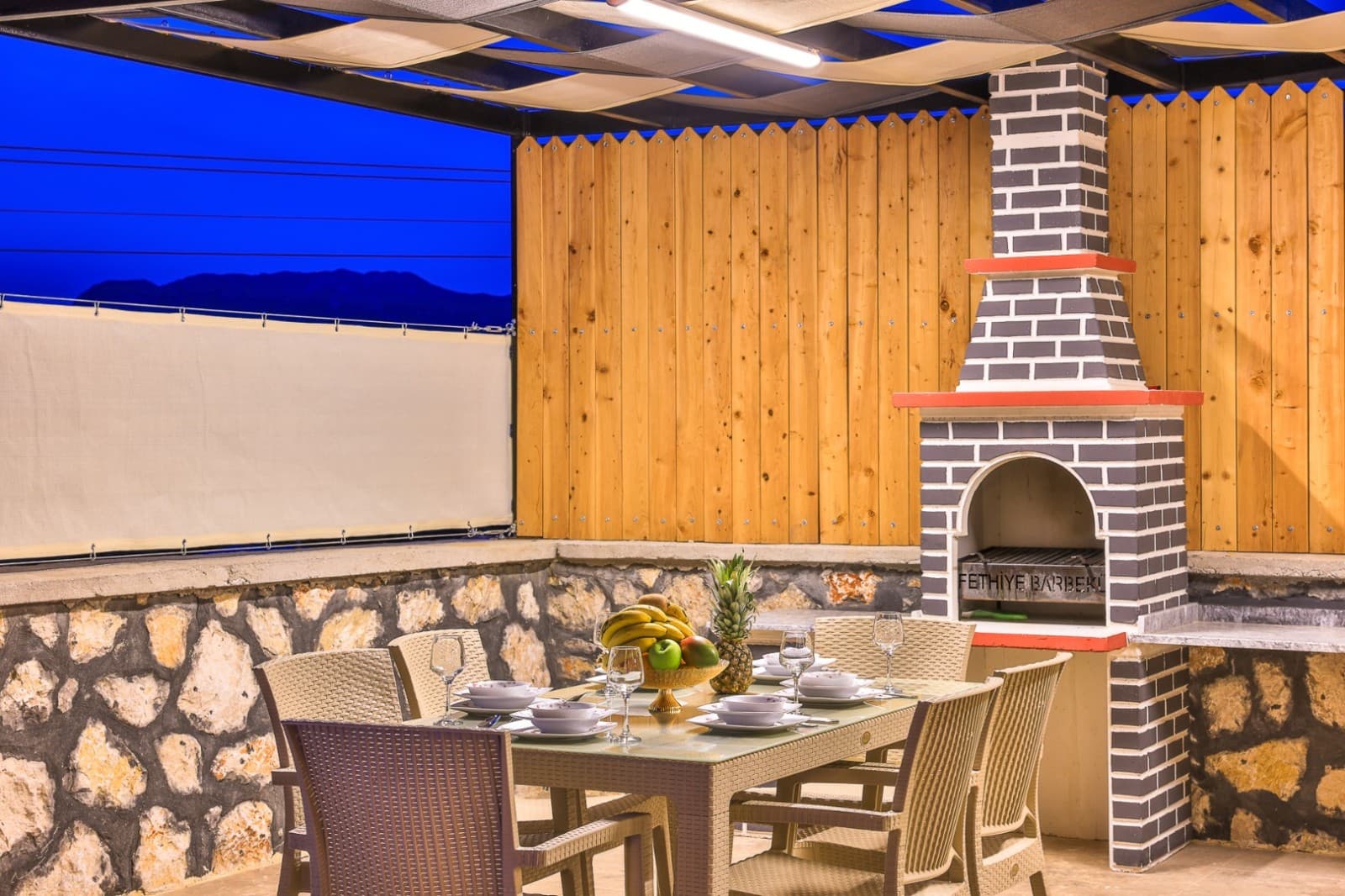 Açık havada barbekü köşesi önünde servis açılmış ahşap yemek masası.