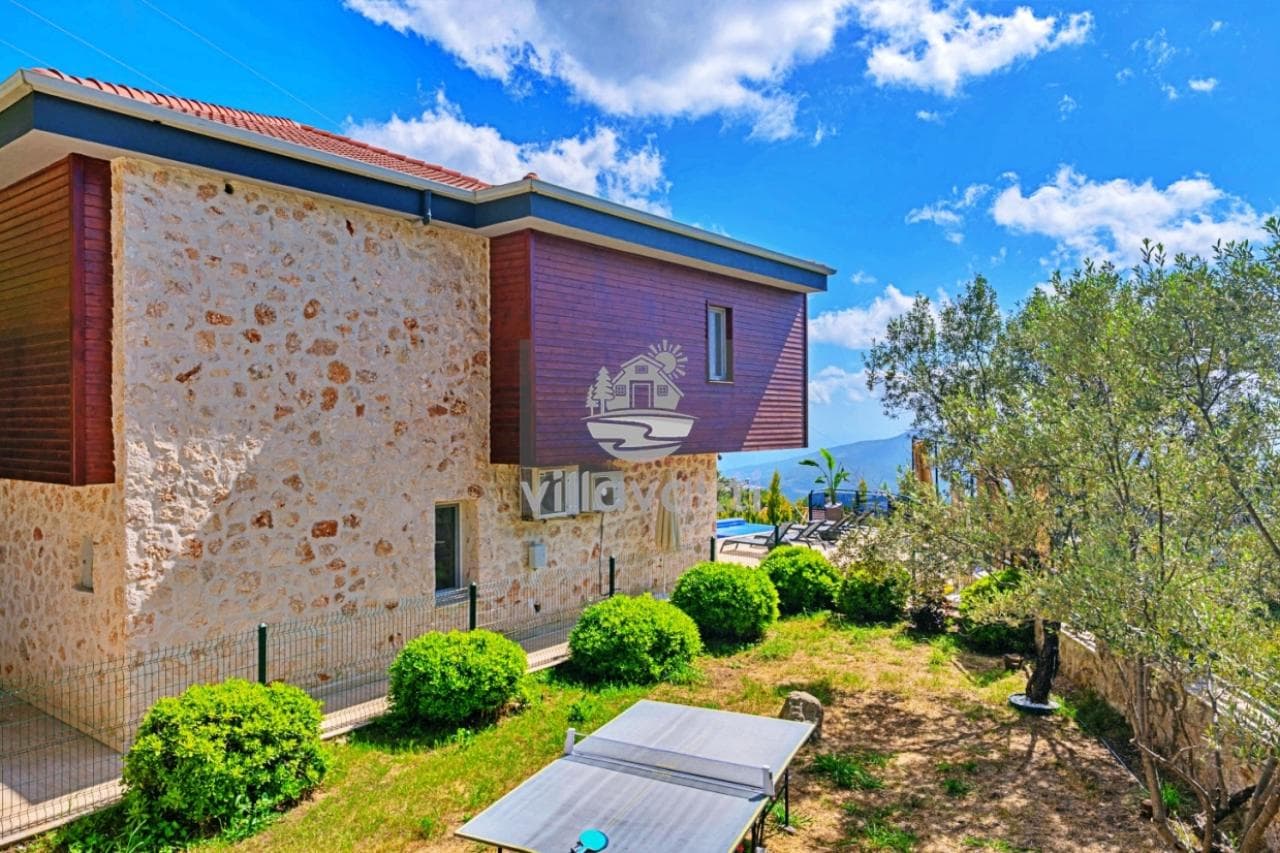 Taş kaplama dış cepheye sahip villa, bahçesinde masa tenisi ve zeytin ağaçları yer alıyor.