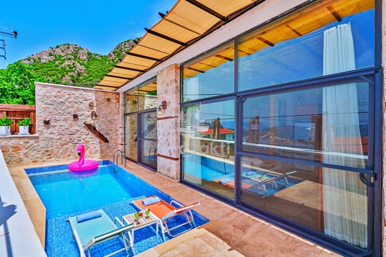 Taş duvarlı, cam kapılı villa önünde pembe flamingo deniz yatağı bulunan küçük havuz.