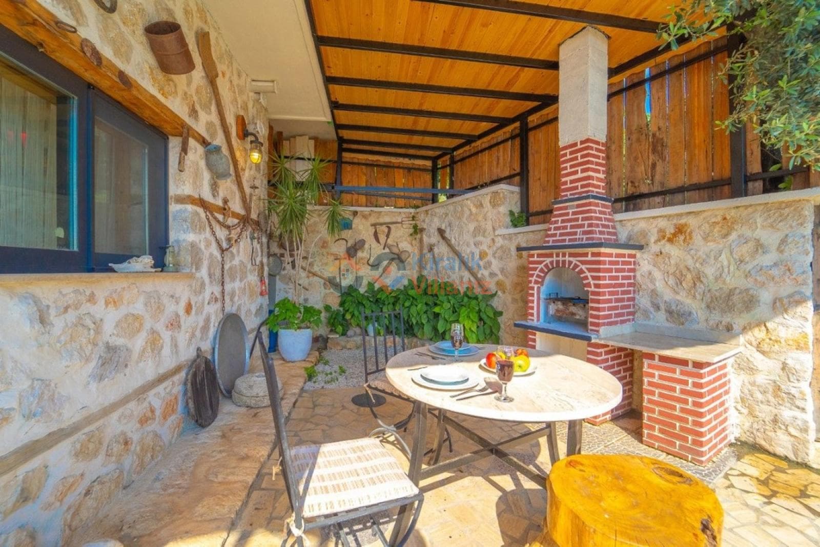 Taş duvarlı, tuğla barbekülü ve ahşap tavanlı, dış mekanda yemek masası bulunan veranda.