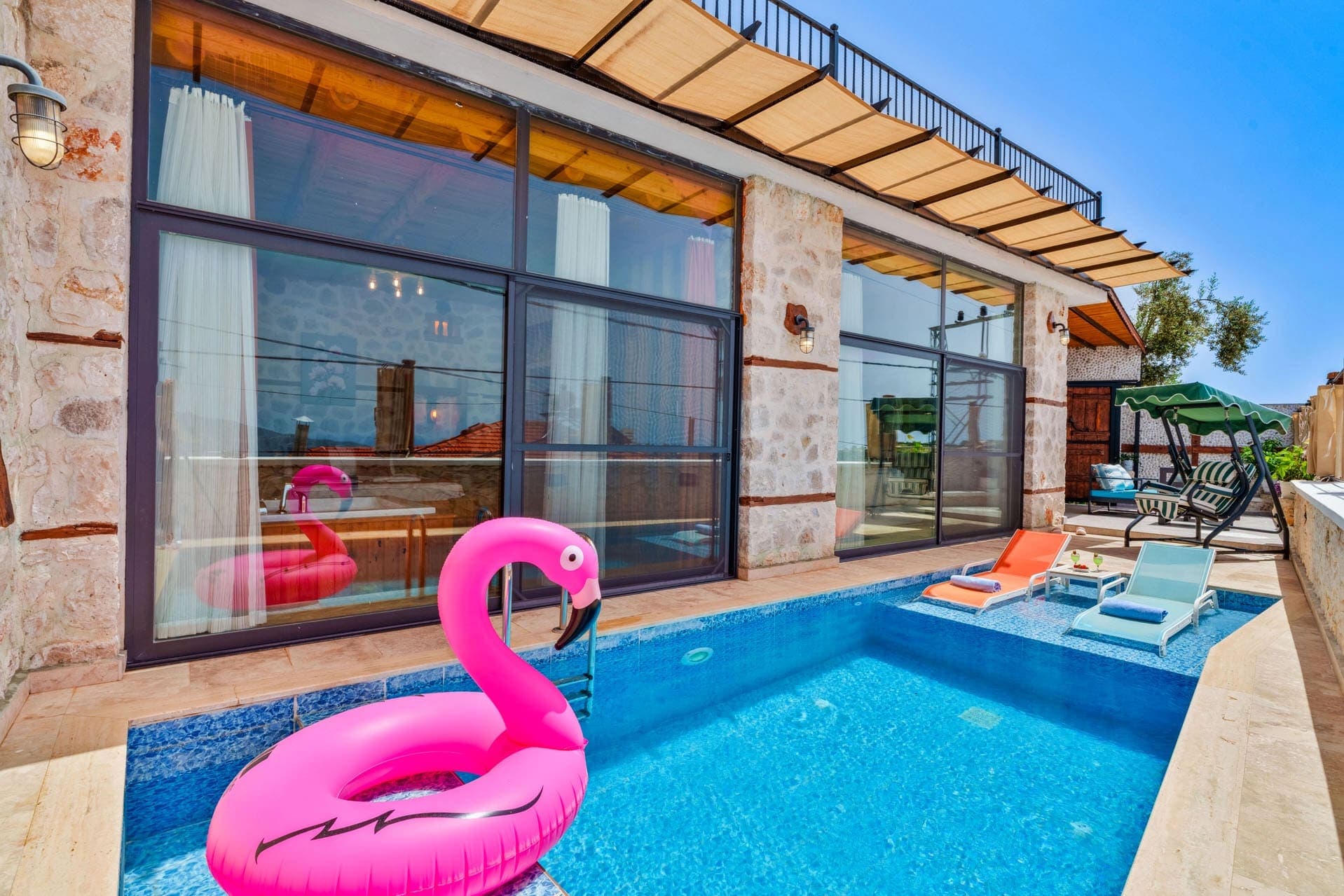 Pembe flamingo deniz yatağı ve şezlonglar bulunan, taş duvarlı villanın önündeki havuz.