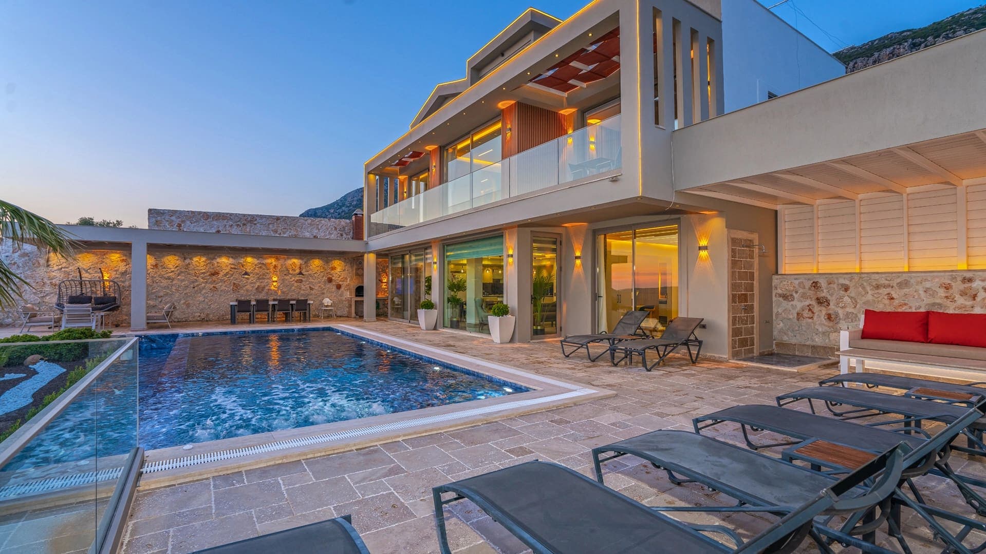 Akşam ışıklandırmalı, havuz kenarında şezlonglar bulunan modern dış cepheli villa.