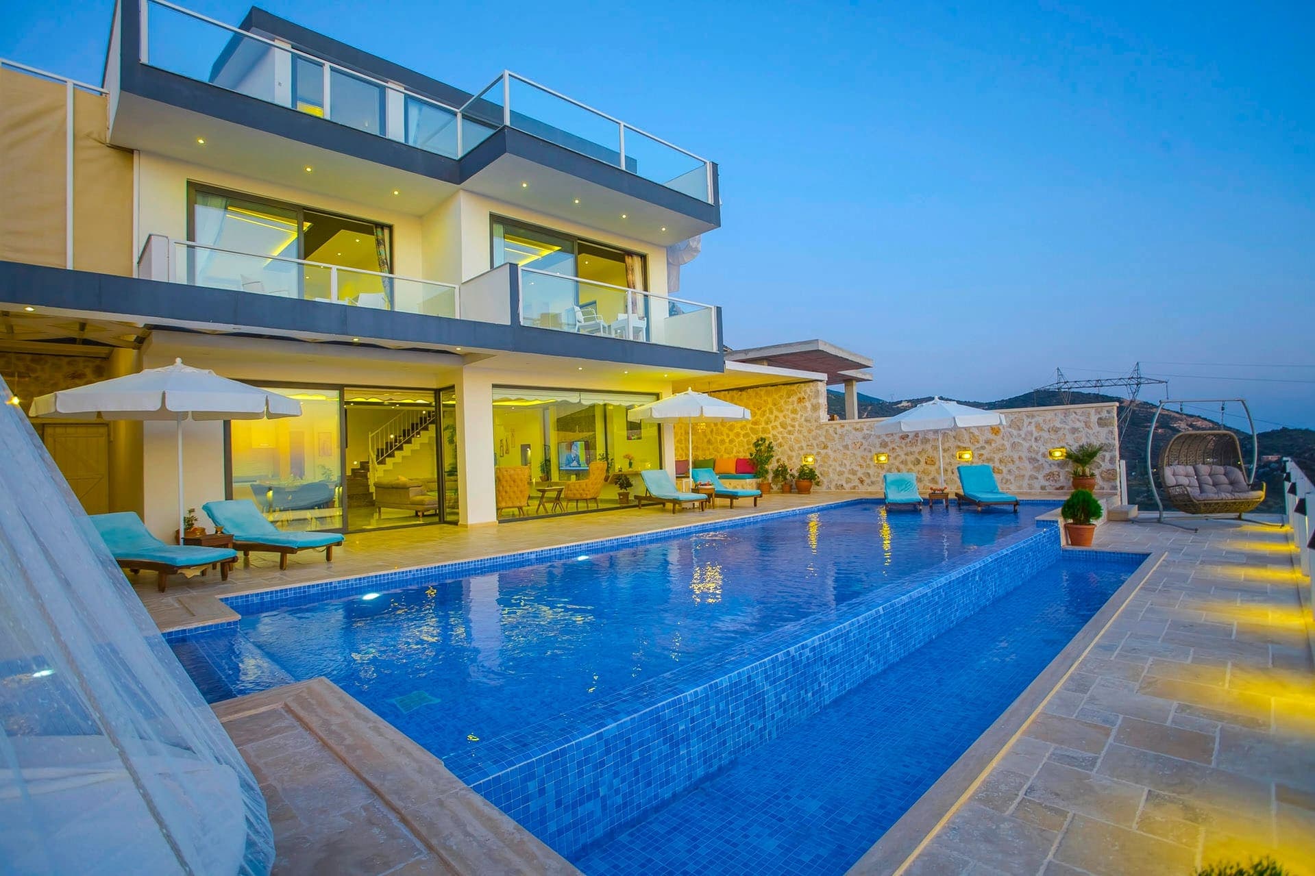 Mavi havuzlu, şezlonglu ve güneş şemsiyeli, iki katlı modern bir villa.