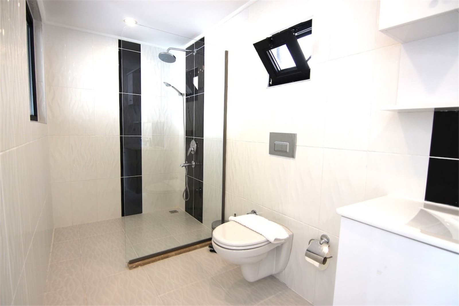 Duş alanı, asma klozet ve lavabo bulunan beyaz fayanslı modern banyo.