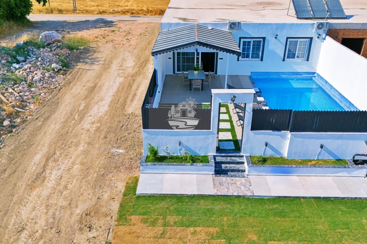 Beyaz dış cepheli, havuzlu, küçük verandalı ve toprak zeminli bahçesi olan villa.