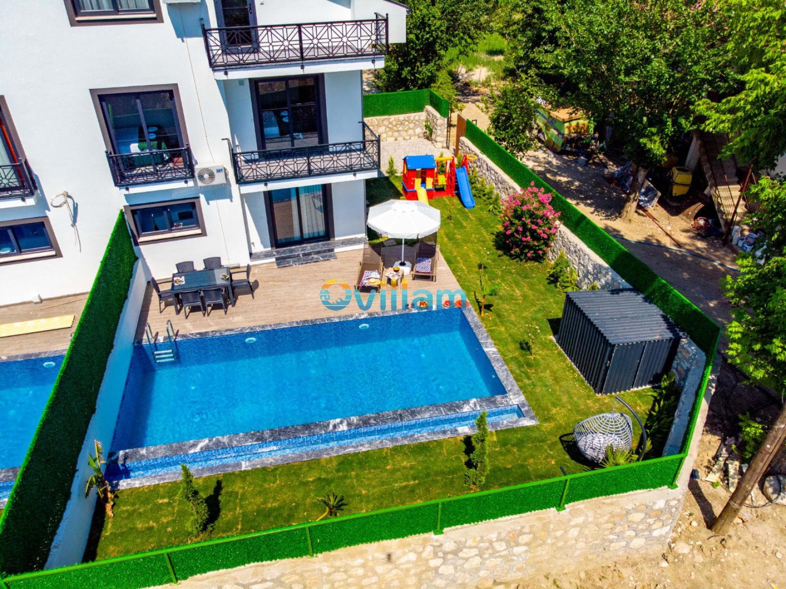 Havuzlu villanın kuş bakışı görünümü, bahçede çocuk oyun alanı ve yemek masası.