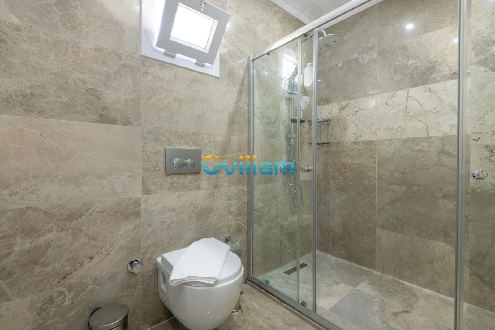 Bej mermer kaplı, cam duşakabinli ve asma klozetli modern banyo.
