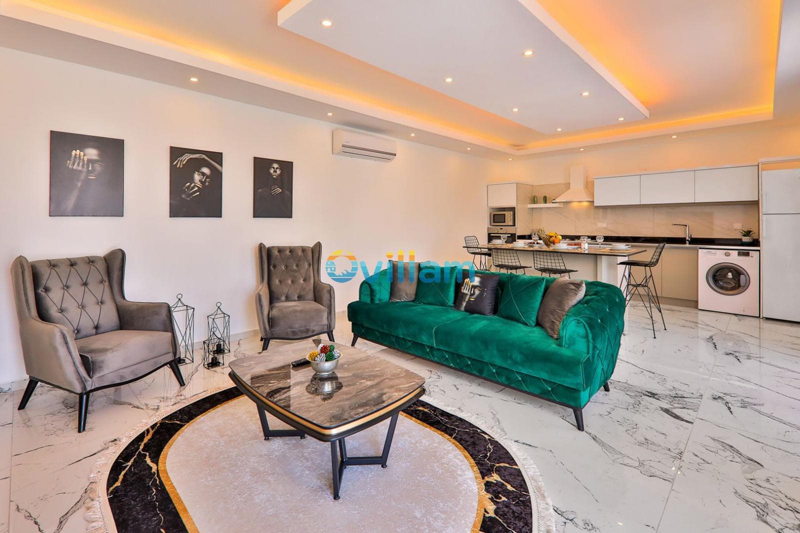 Yeşil kadife koltuklu, mermer zeminli, modern mutfaklı açık konsept salon.