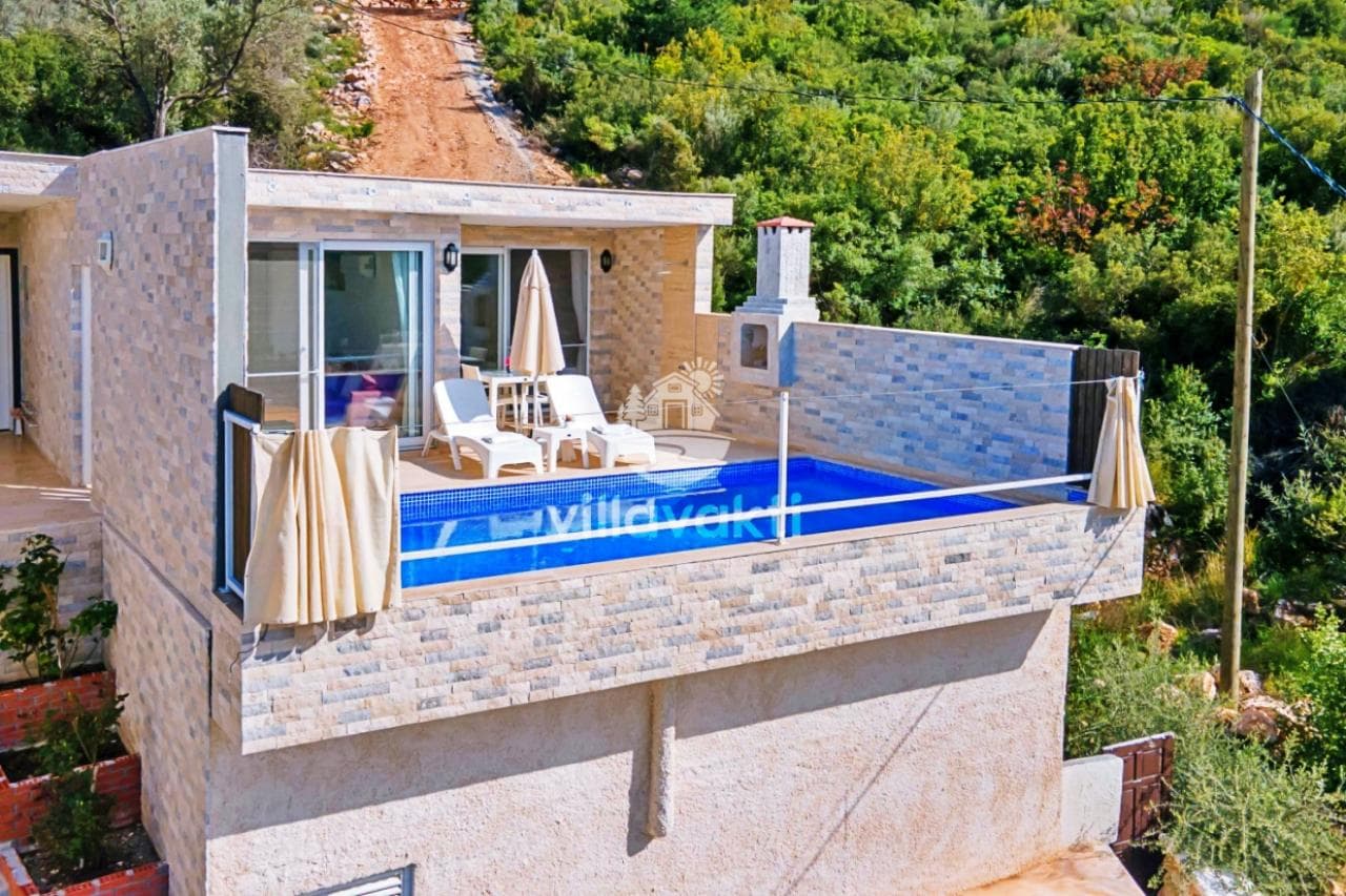 Taş kaplama dış cepheye sahip, önünde özel havuzu ve şezlongları bulunan güneşli villa terası.